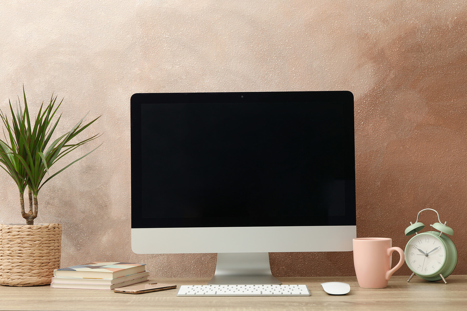 Workplace with computer, plant and alarm clock on wooden table.