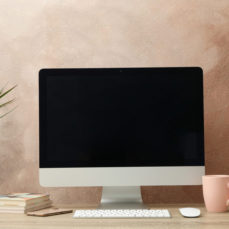 Workplace with computer, plant and alarm clock on wooden table.