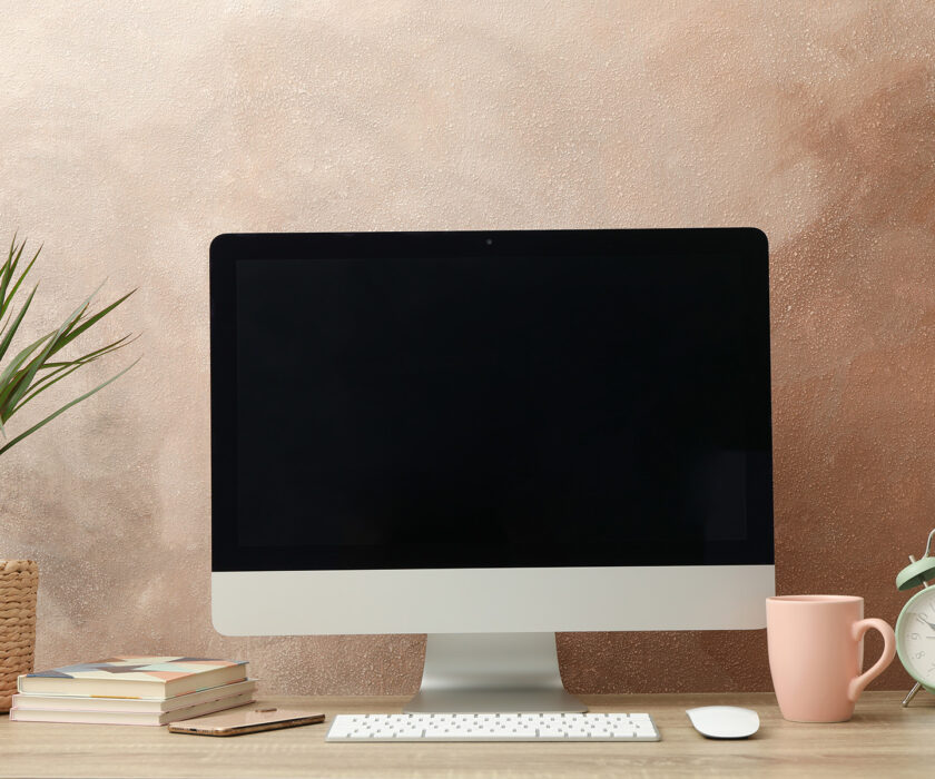 Workplace with computer, plant and alarm clock on wooden table.